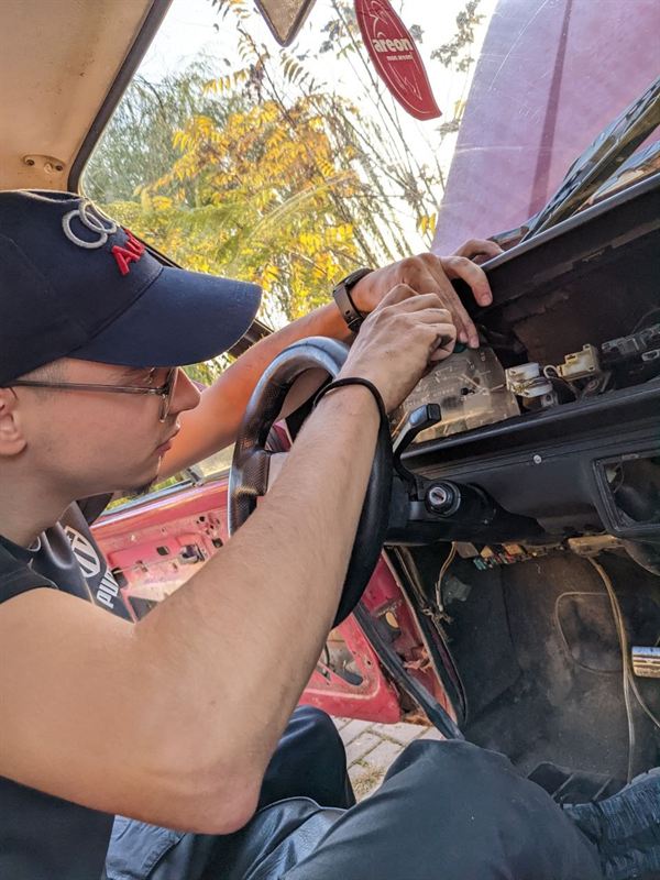 Fatih working on the wiring behind a car's dashboard.