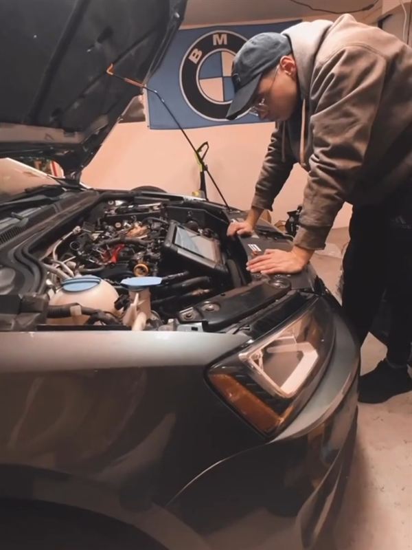 Fatih leaning into a car's engine bay in a garage.