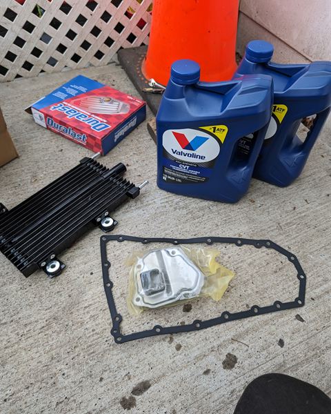 New transmission cooler, filter, pan gasket and bottles of CVT fluid laid out for the job.
