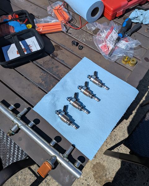 Fuel injectors laid out on a towel with new seals, next to the fuel rail.