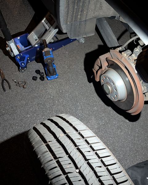 Car raised on a jack with the wheel off, the tire on the ground beside it.